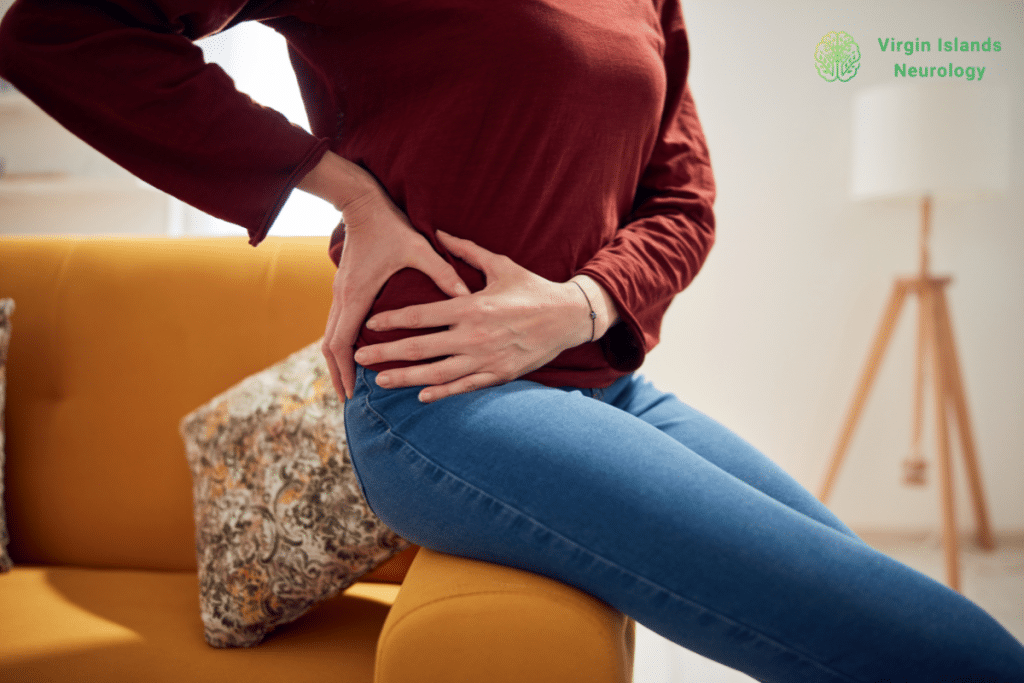 A woman sitting on the arm rest of a couch holding her hip in pain in the U.S Virgin Islands.